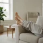 Entspannte Beine einer Person, die zur Entlastung leicht erhöht auf dem Sofa gelagert sind.